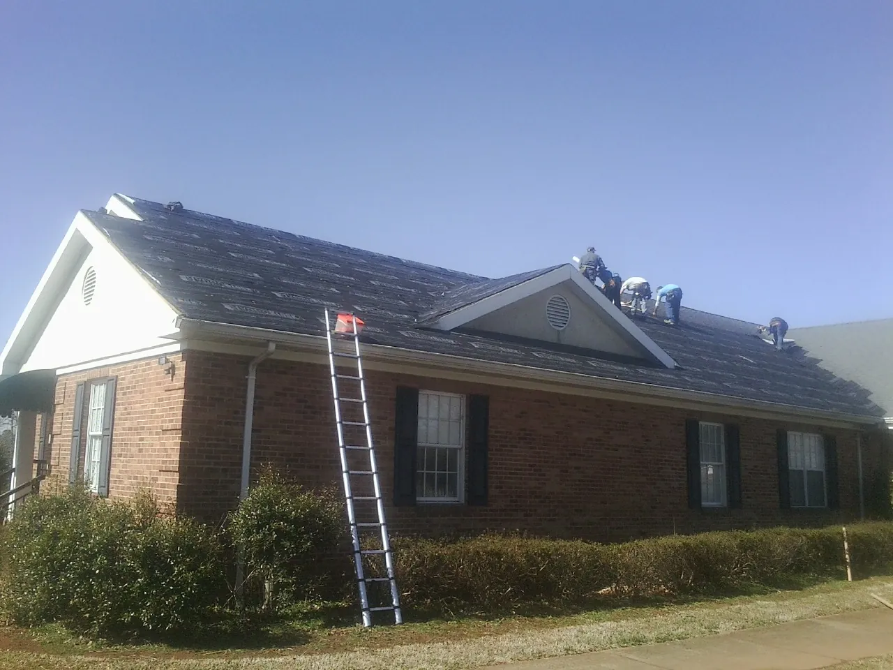 Crew tearing shingles off a brick ranch roof with a ladder set — Emergency Roof Repair work by our crew in Risingsun
