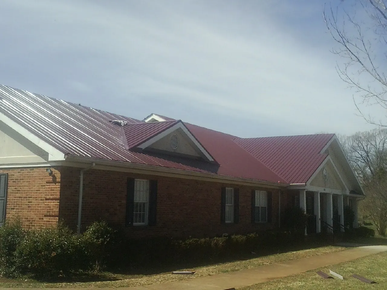 Red metal roof with gabled entries on a long brick building, from a Hail Damage Roof Repair job in Risingsun