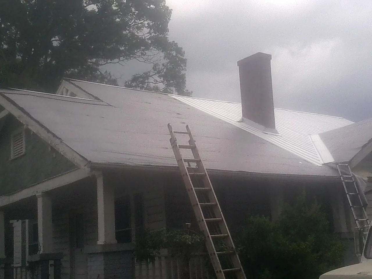 Ladders against a metal roof on an older home with a brick chimney in Risingsun