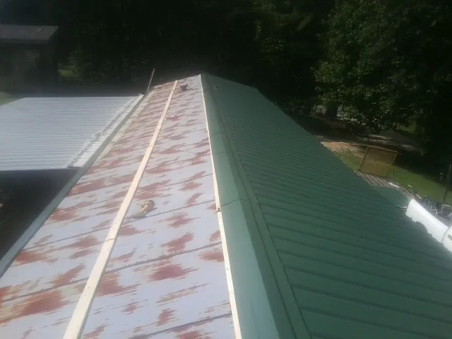Old rusted panels beside newly installed green metal roofing — Wind Damage Roof Repair by Roofing Brothers in Risingsun