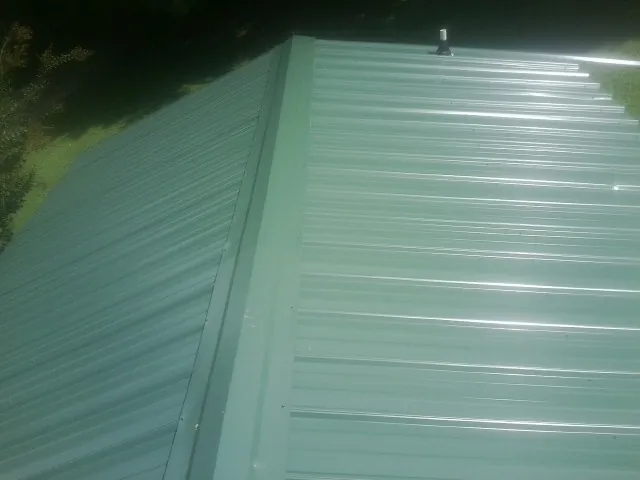 New green metal panels meeting at the ridge of a roof — Flat Roof Repair work by our crew in Risingsun