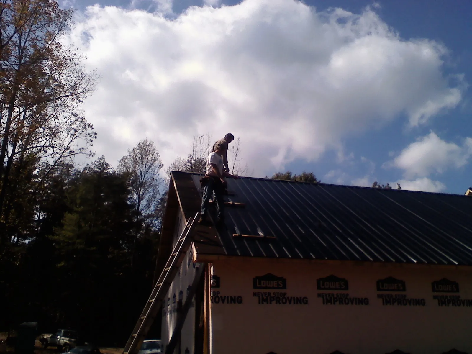 Roofer fastening dark metal panels high against a cloudy sky, from a Roof Inspection job in Risingsun