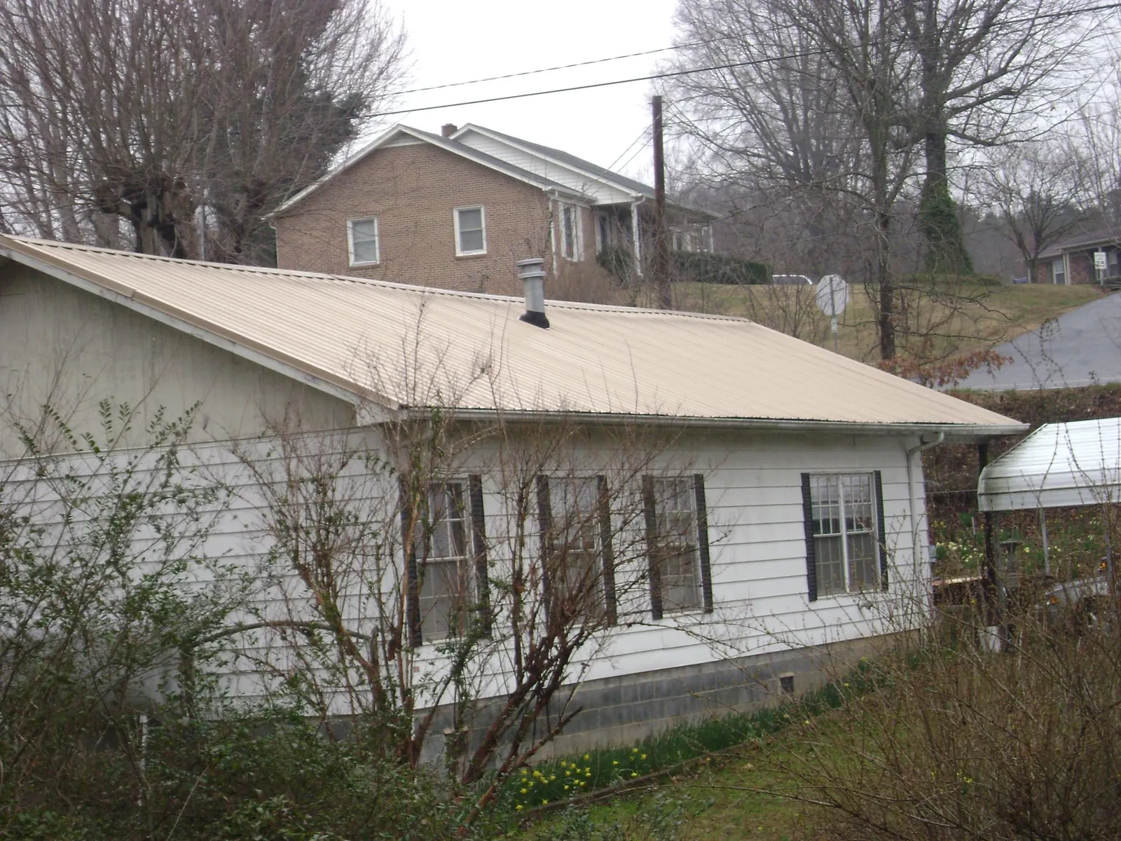 Tan metal roof on a white sided house set into a hillside — Commercial Roofing by Roofing Brothers in Risingsun